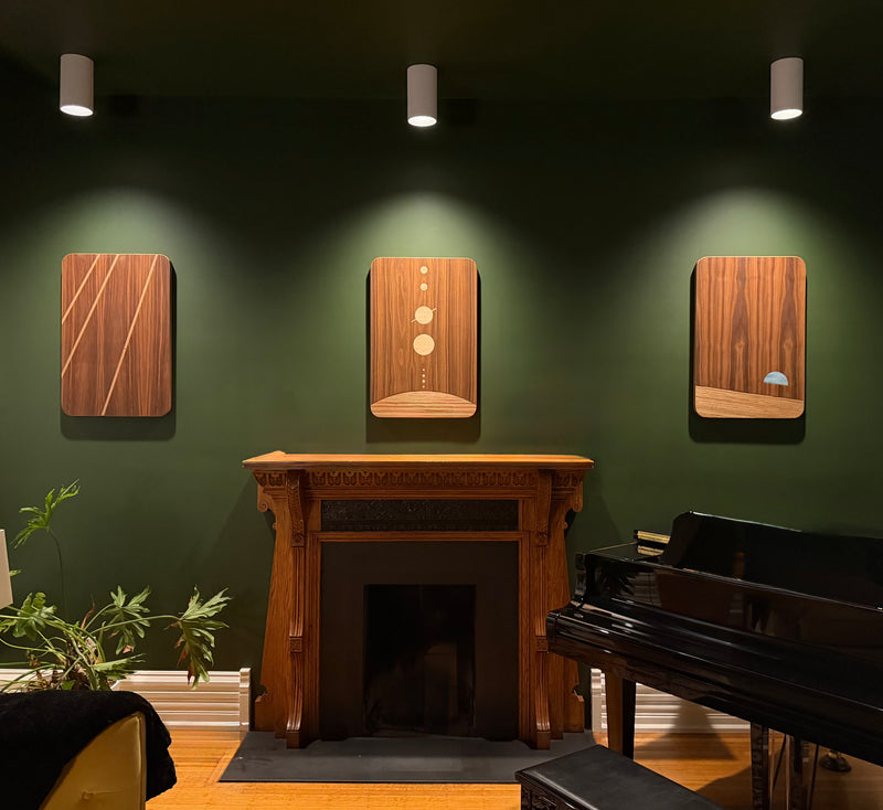 three wood wall hangings with earth in blue staged with downlight in a green den or sitting room above a fireplace and grand piano